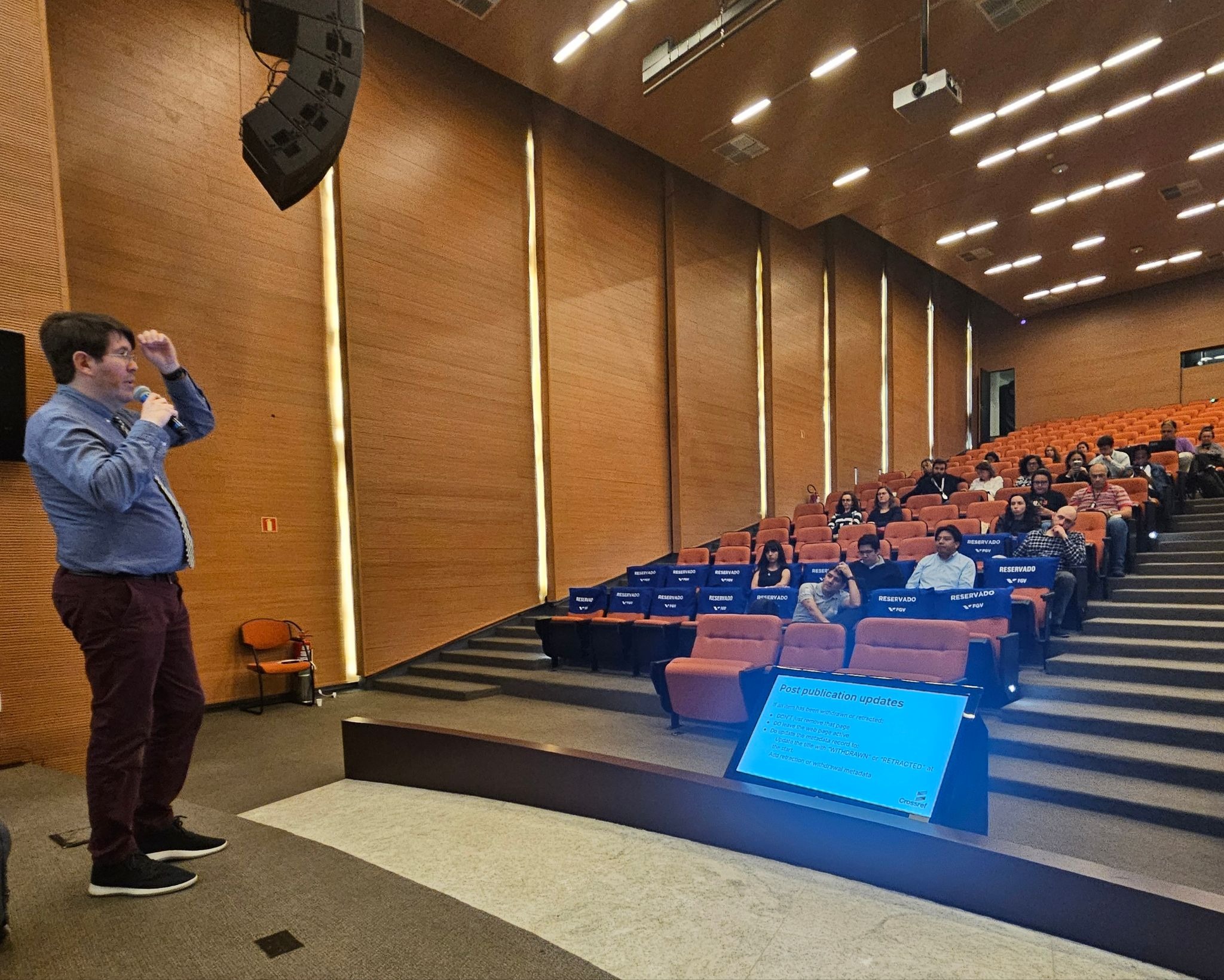 Speaker presenting to an audience at Crossref São Paulo, discussing metadata updates.